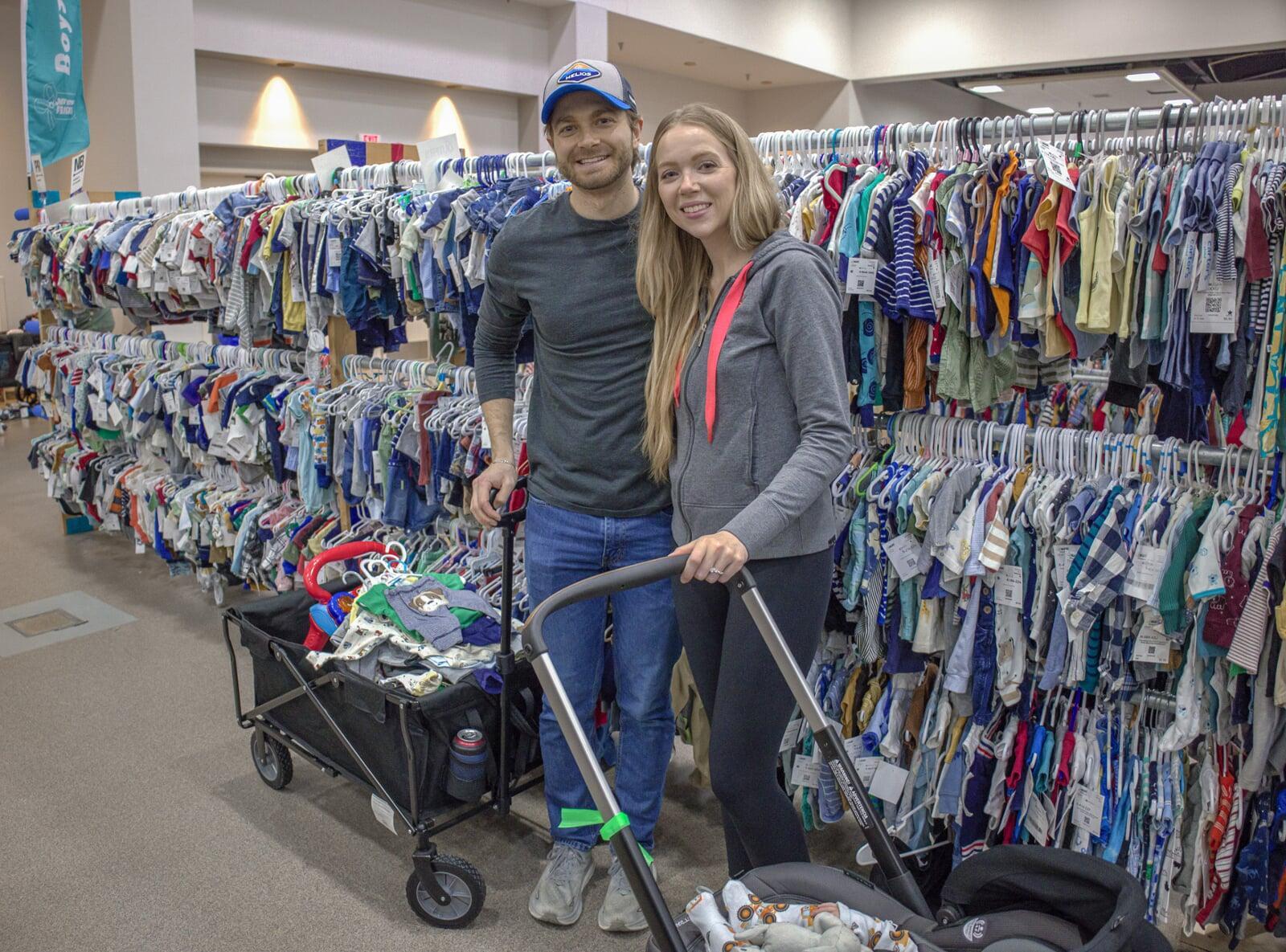 A young JBF shopper mom in a black Metallica T-shirt holds an outfit she intends to buy at her local JBF sale.