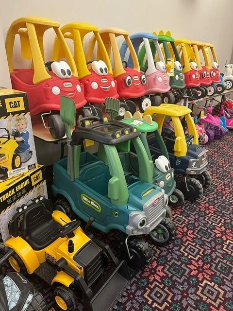 Tricycles, scooters and toys lined up on a table waiting for shoppers to attend the sale.